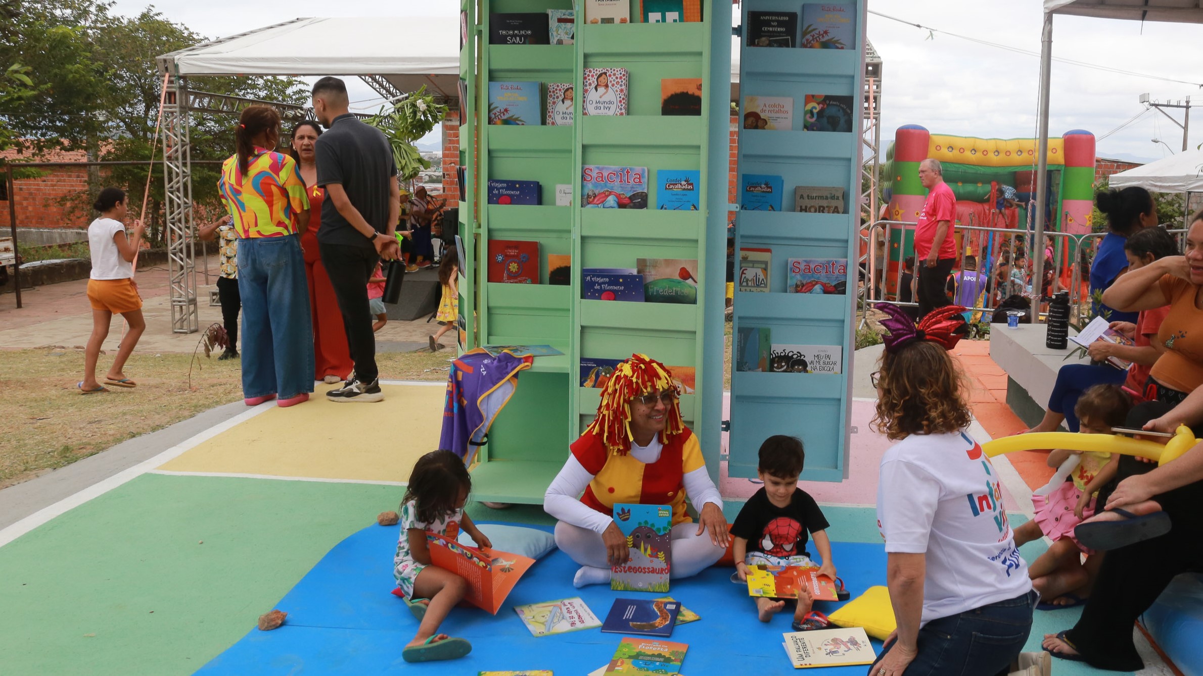 quiosque de livros do leitura na praça com uma mulher vestida de Emília do Sítio do Pica-pau Amarelo lendo livros para duas crianças